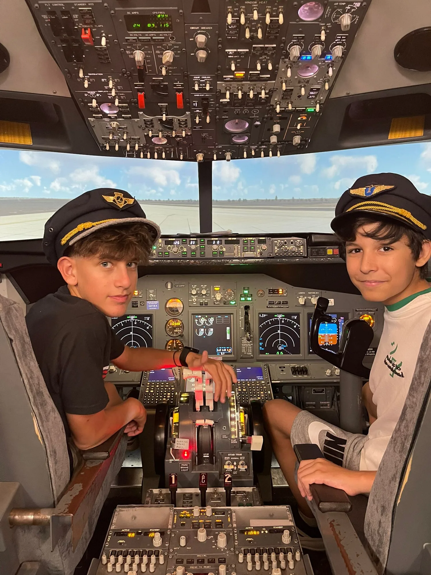 Two boys wearing pilot caps in the Boeing simulator cockpit
